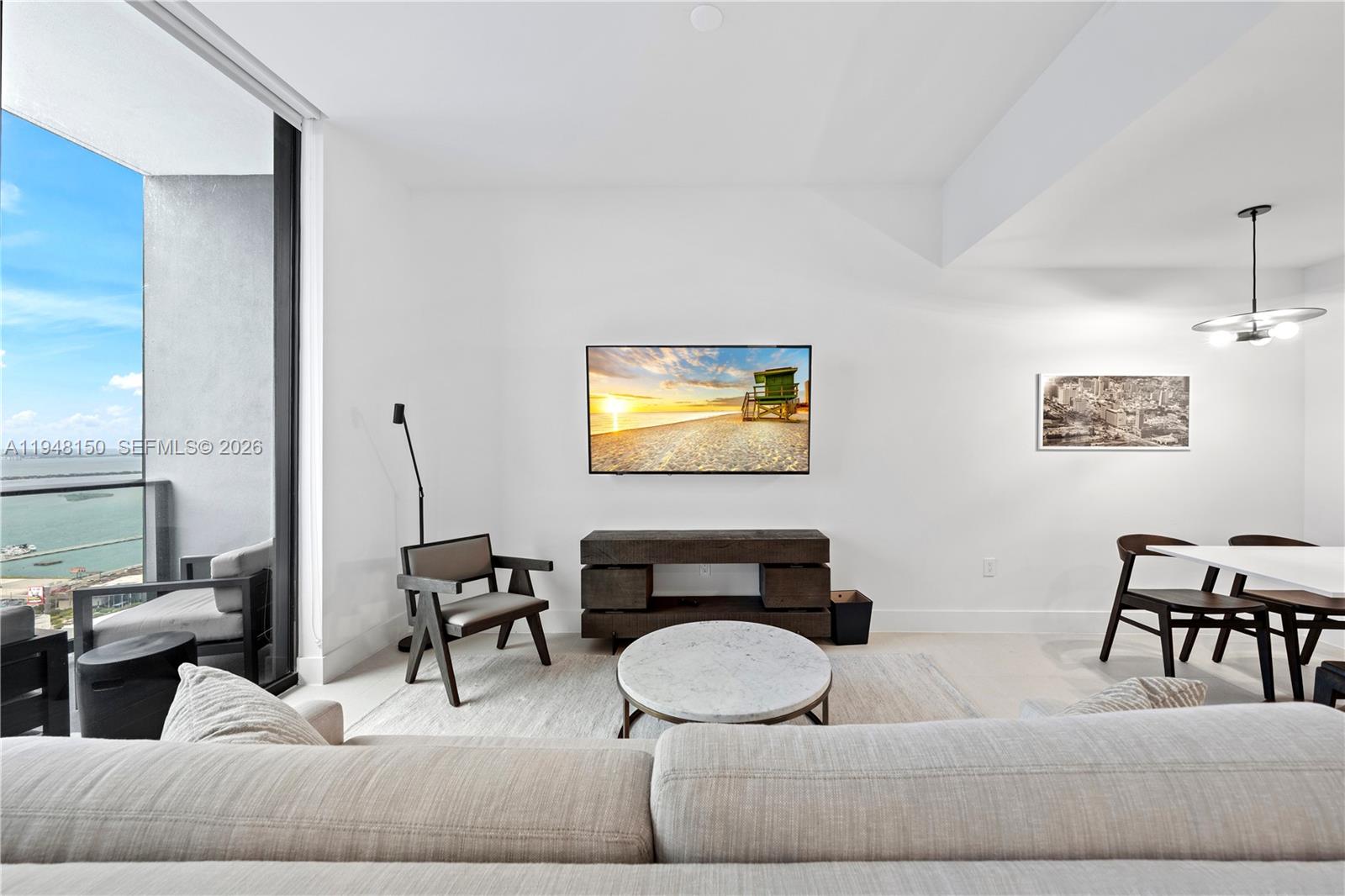 A living room features a wall-mounted television, a wooden console, and a balcony with water views — 159 NE 6th St # 5113, Miami FL 33132, MIAMI, FL