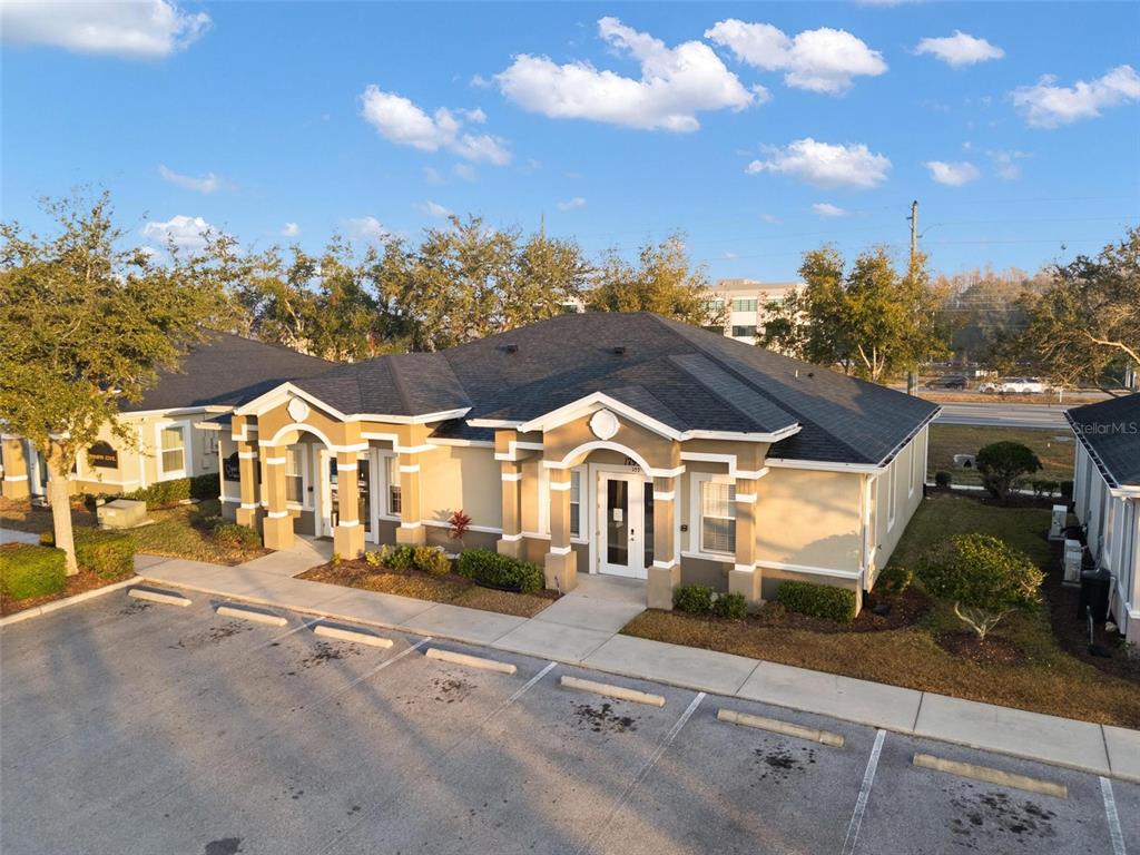 An exterior view of a tan commercial building with a dark shingled roof and parking — 17929 HUNTING BOW CIRCLE UNIT 101 & 102, LUTZ, FL