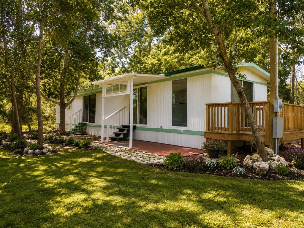 A white mobile home features a wooden deck, a covered patio, and surrounding trees — 8010 W MORROW COURT, CRYSTAL RIVER, FL