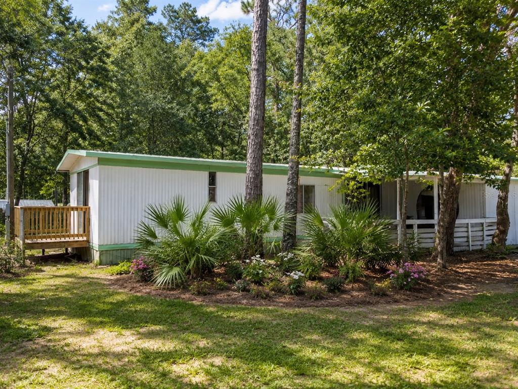 A white mobile home with a green trim and a wooden deck sits among trees — 8010 W MORROW COURT, CRYSTAL RIVER, FL