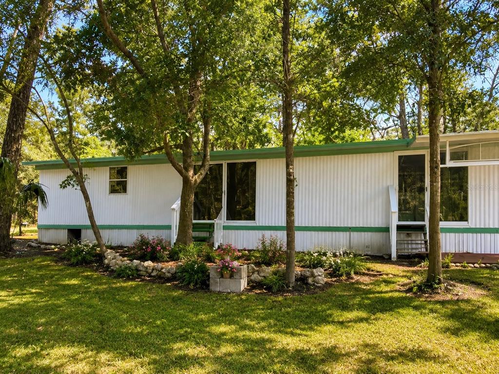 A white mobile home with green trim sits in a yard with trees and landscaping — 8010 W MORROW COURT, CRYSTAL RIVER, FL