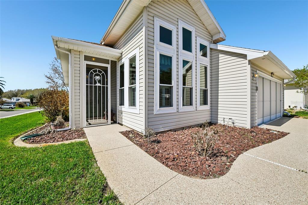 A beige vinyl-sided house features a front door with a decorative screen and tall windows — 6105 DORY WAY, TAVARES, FL