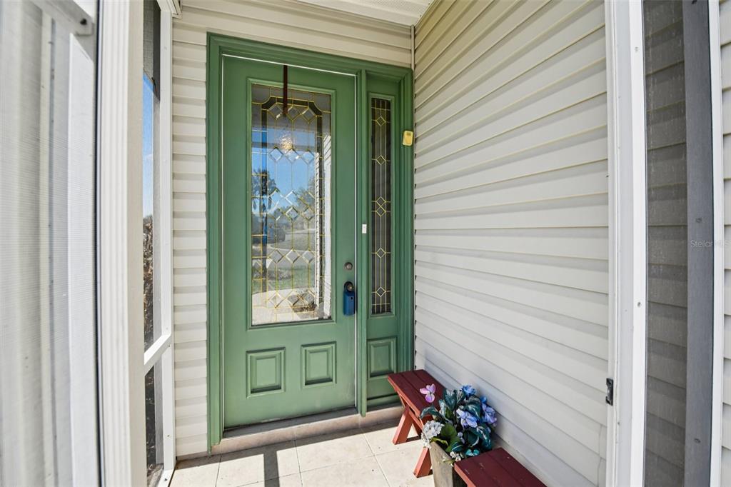 A green front door with a glass insert and sidelight sits on a tiled porch — 6105 DORY WAY, TAVARES, FL