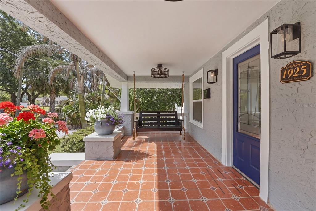 A covered porch features terracotta tile flooring, a hanging bench, and a blue front door — 204 N BROWN AVENUE, ORLANDO, FL