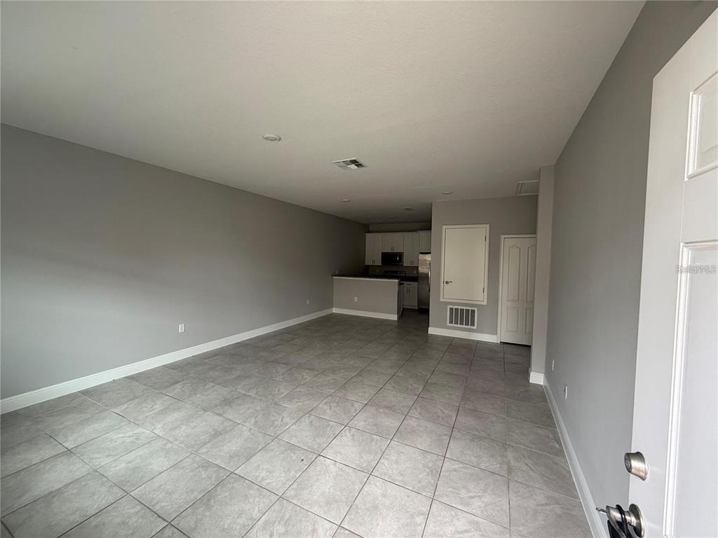 An open-concept living area features gray walls, tiled floors, and a kitchen in the background — 1789 CORIANDER DRIVE, KISSIMMEE, FL