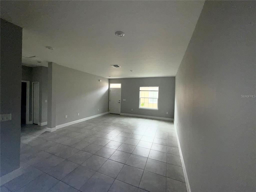 An empty room with gray walls, light-colored tile flooring, a front door, and a window — 1789 CORIANDER DRIVE, KISSIMMEE, FL