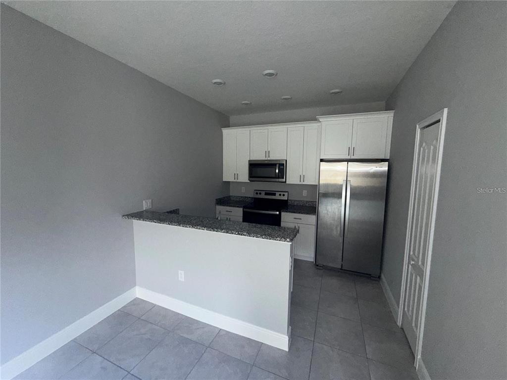 A kitchen features white cabinets, stainless steel appliances, granite countertops, and a breakfast bar — 1789 CORIANDER DRIVE, KISSIMMEE, FL