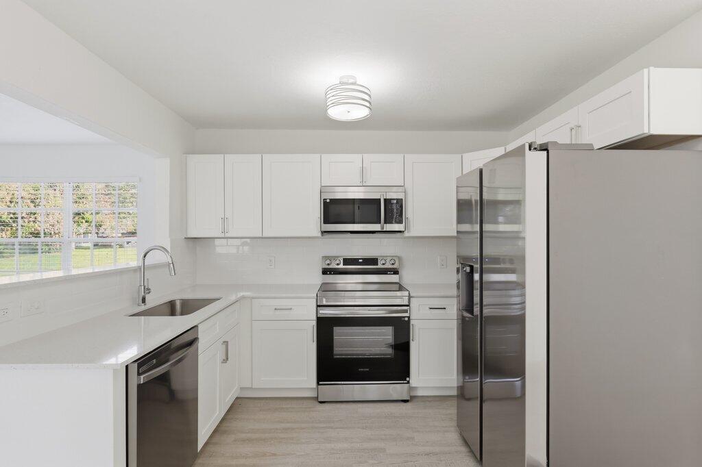 A modern kitchen features white cabinets, stainless steel appliances, and light-colored countertops — 2521 SE Berkshire Boulevard, FL 34952, FL