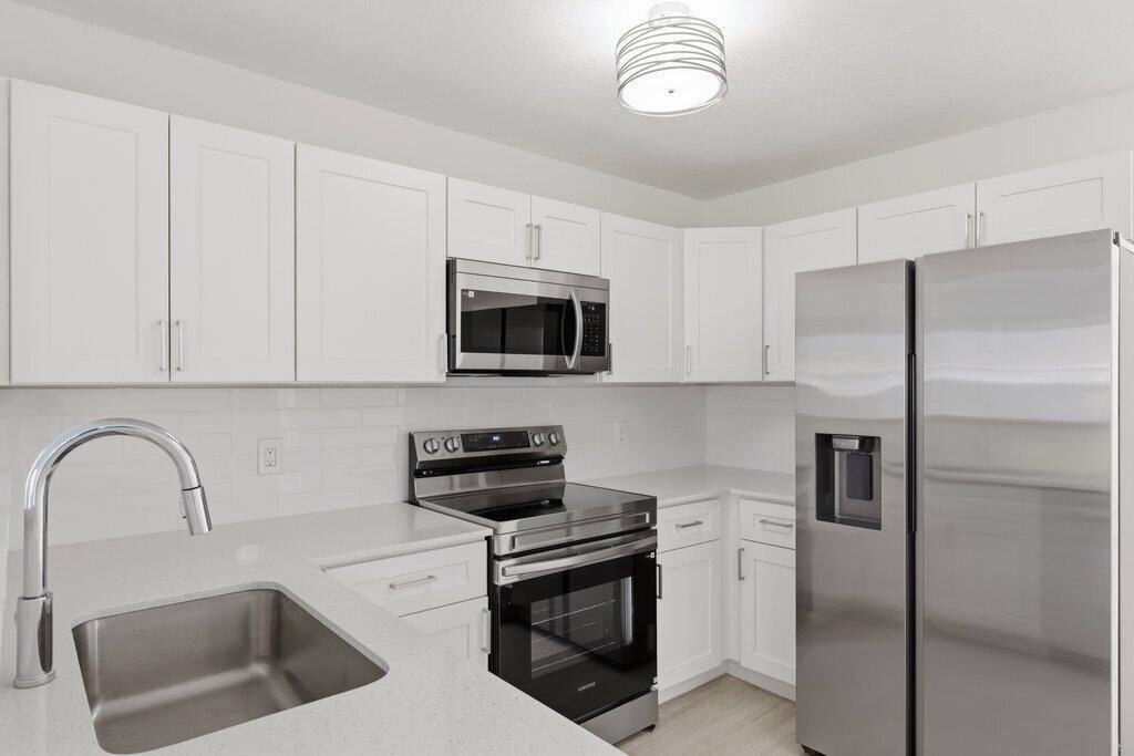 A modern kitchen features white cabinets, stainless steel appliances, and light-colored quartz countertops — 2521 SE Berkshire Boulevard, FL 34952, FL