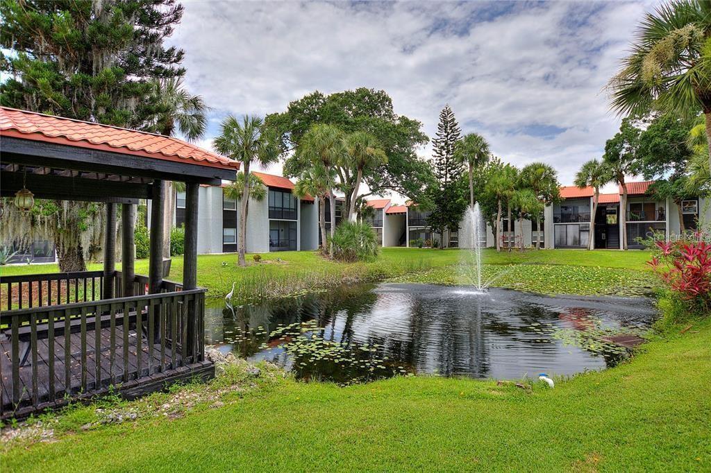 A gazebo overlooks a pond with a fountain in front of multi-story apartment buildings — 3215 BENEVA ROAD UNIT 204, SARASOTA, FL