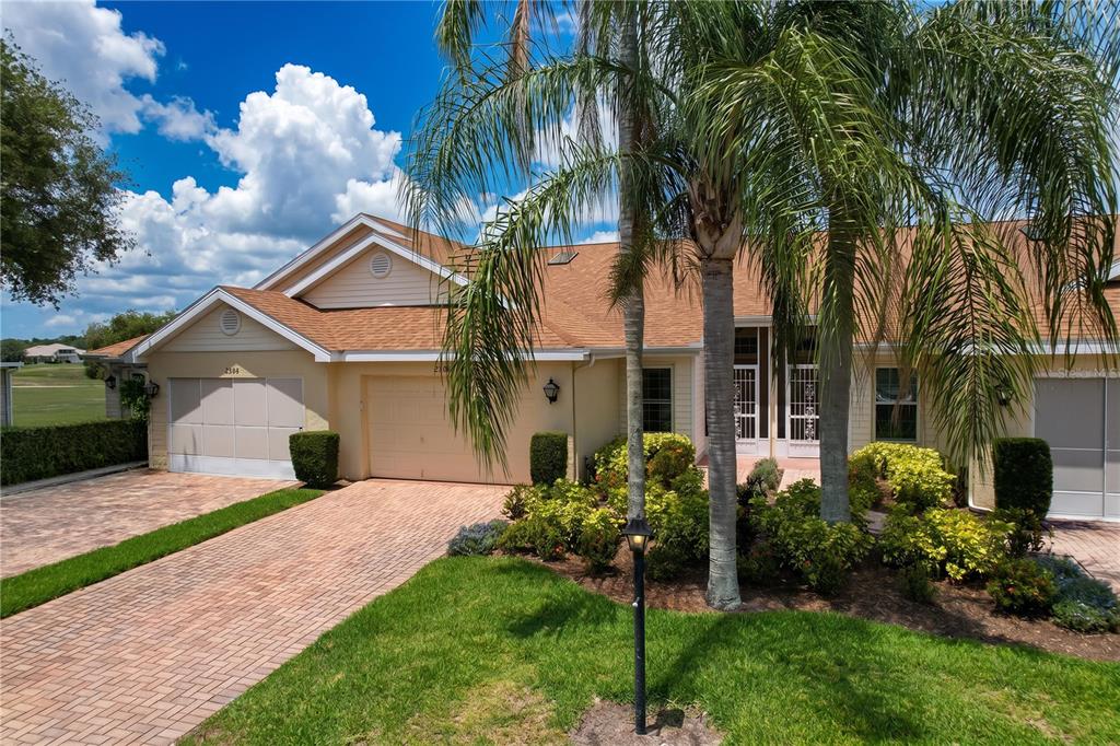 A tan house with a brick driveway, palm trees, and a multi-gabled shingled roof — 2307 NEW ORCHARD COURT, SUN CITY CENTER, FL