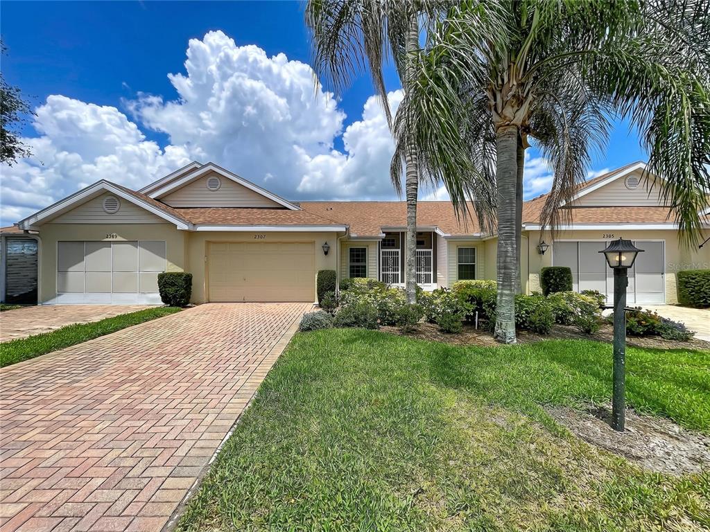 A single-story residential building with a brick driveway, palm tree, and three garage doors — 2307 NEW ORCHARD COURT, SUN CITY CENTER, FL