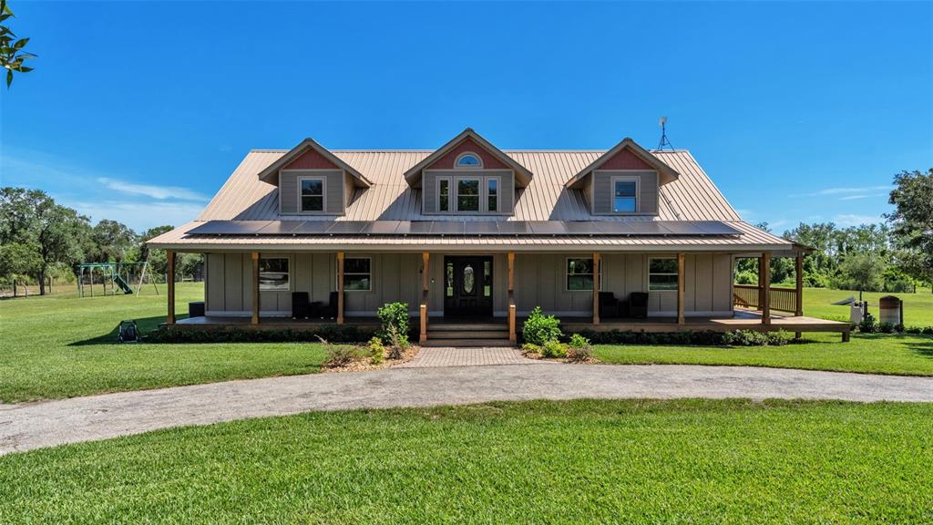 A tan farmhouse with a metal roof, solar panels, and a wide front porch — 339 MINI RANCH ROAD, SEBRING, FL