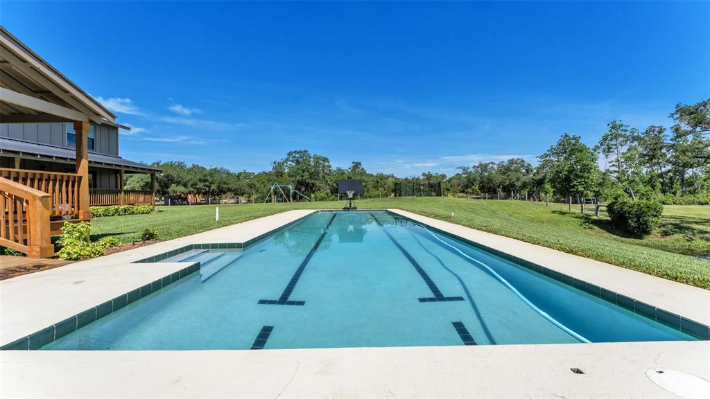 A long rectangular swimming pool sits in a grassy backyard next to a wooden deck — 339 MINI RANCH ROAD, SEBRING, FL