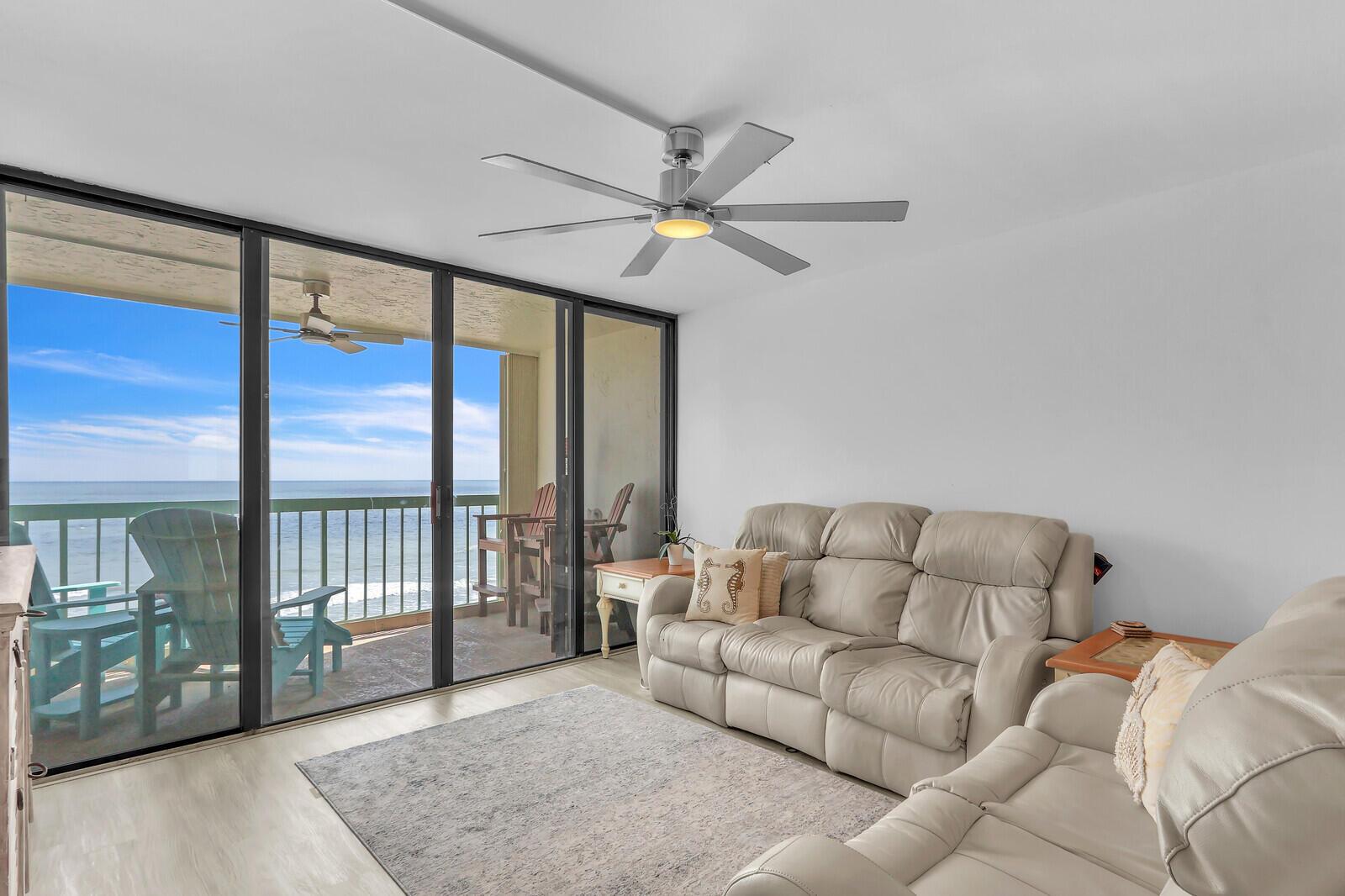 A living room with light-colored leather sofas, a ceiling fan, and a balcony overlooking the ocean — 9900 S Ocean Drive # 804, Jensen Beach FL 34957, JENSEN BEACH, FL