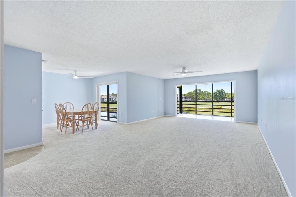 A spacious living and dining area with light blue walls, beige carpeting, and large windows — 5194 MARSH FIELD LANE UNIT 96, SARASOTA, FL