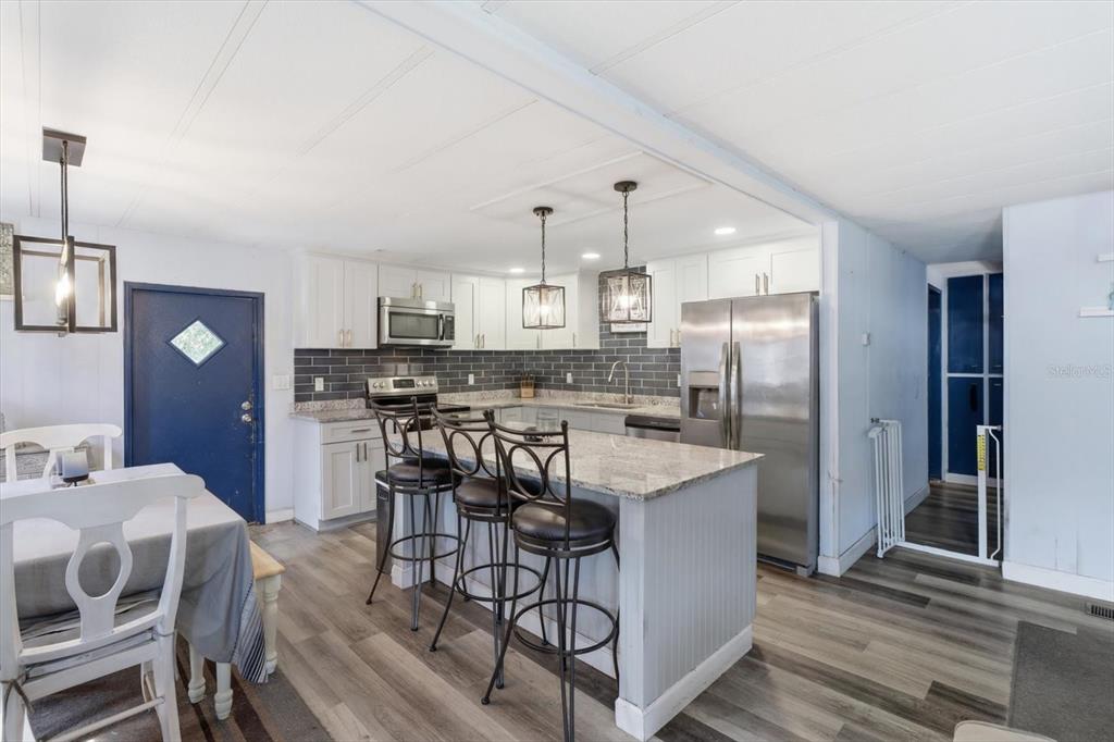 A kitchen features white cabinets, a granite island with three stools, and gray tile backsplashes — 4610 E AMHERST STREET, HERNANDO, FL