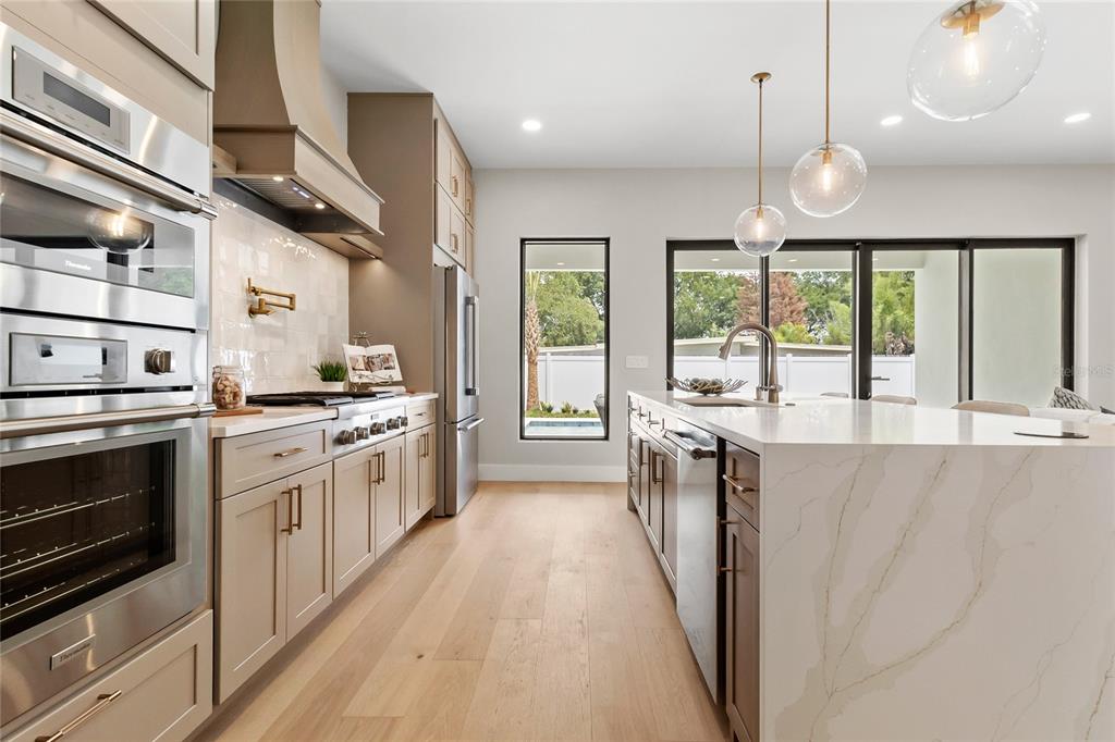 A modern kitchen features light-toned cabinetry, a marble-topped island, stainless steel appliances, and wood flooring — 3807 PELICAN LANE, ORLANDO, FL