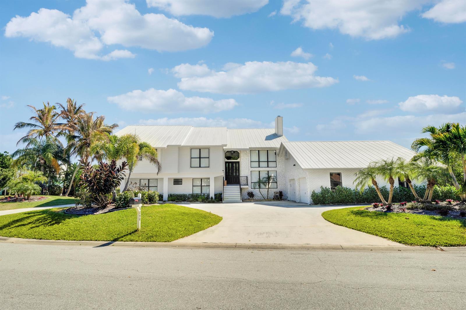 A two-story white brick house with a metal roof and a circular concrete driveway — 4290 SE Whiticar Way, Stuart FL 34997, STUART, FL