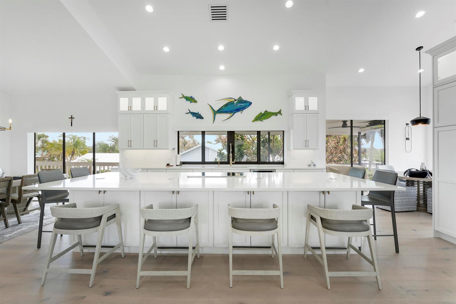 A bright, modern white kitchen features a large island with four chairs and fish wall art — 4290 SE Whiticar Way, Stuart FL 34997, STUART, FL