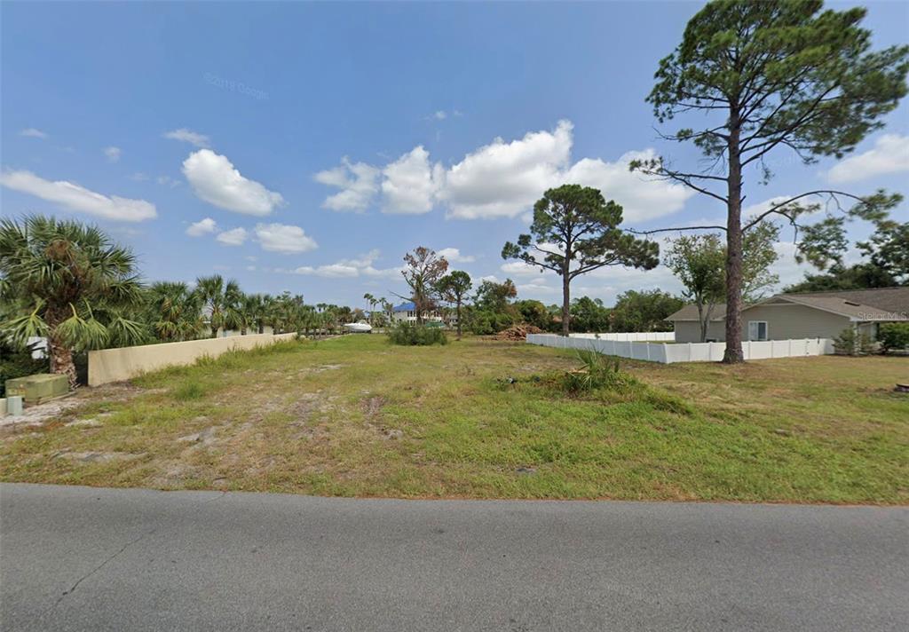 A vacant, grassy residential lot sits between two fenced properties under a blue sky — 475 WAHOO ROAD, PANAMA CITY BEACH, FL