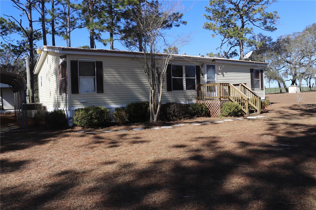 A single-story mobile home with light siding, dark shutters, and a wooden front porch — 2090 SE 133RD COURT, MORRISTON, FL