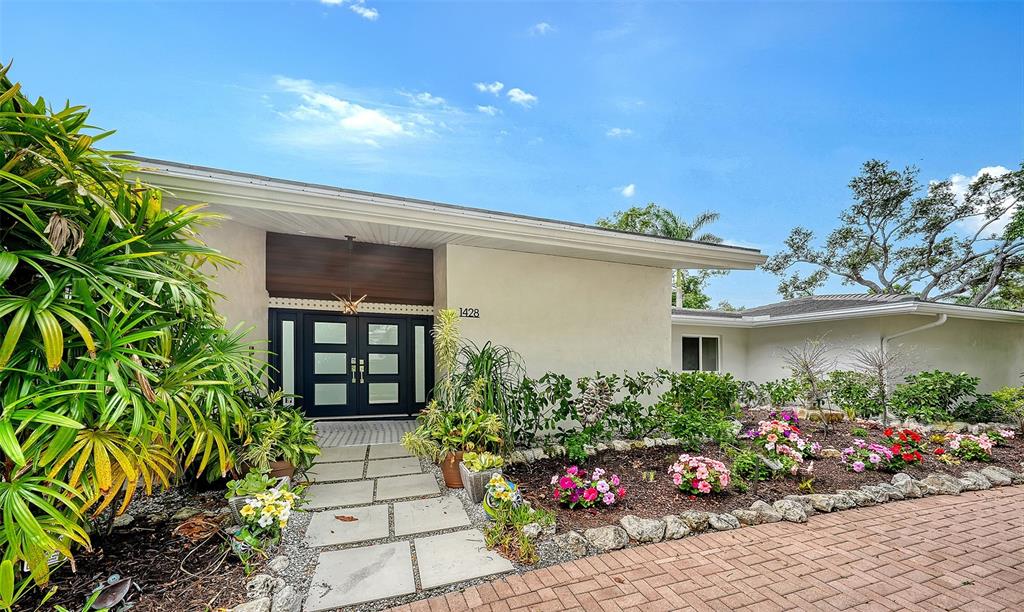 The exterior of a single-story house features a paved walkway leading to a dark double door — 1428 PINE BAY DRIVE, SARASOTA, FL