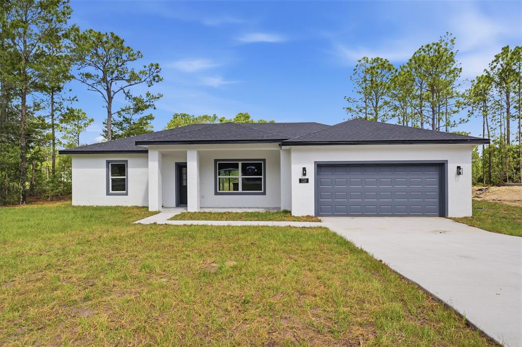 A single-story white house with a dark roof, gray garage door, and surrounding pine trees — 7712 N TIDE POINT, CITRUS SPRINGS, FL
