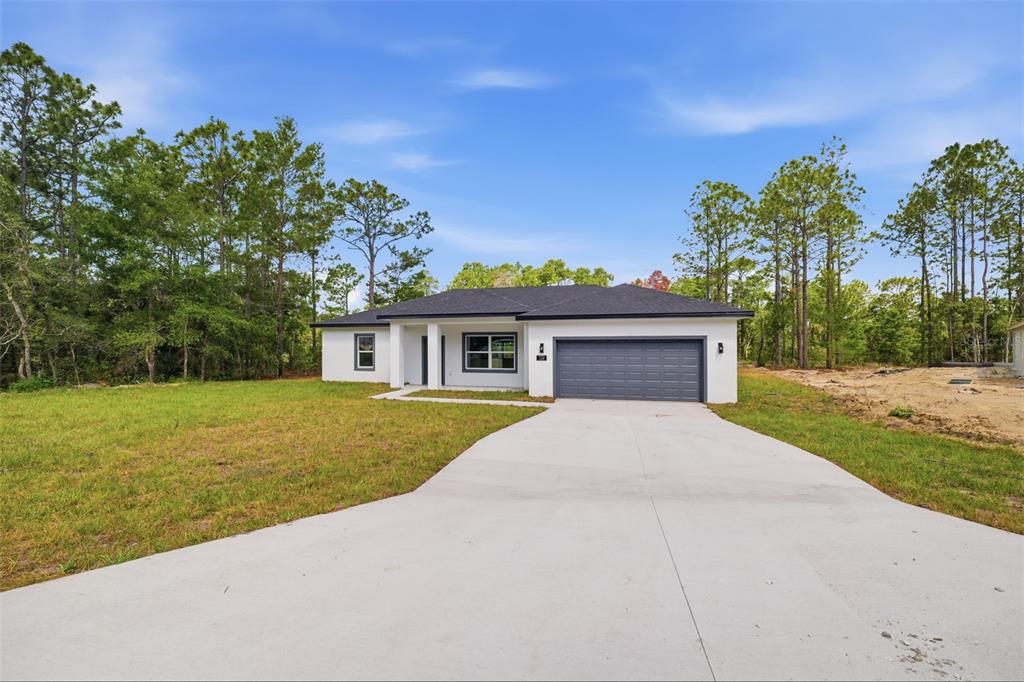 A modern, single-story white house with a gray garage door and a concrete driveway — 7712 N TIDE POINT, CITRUS SPRINGS, FL