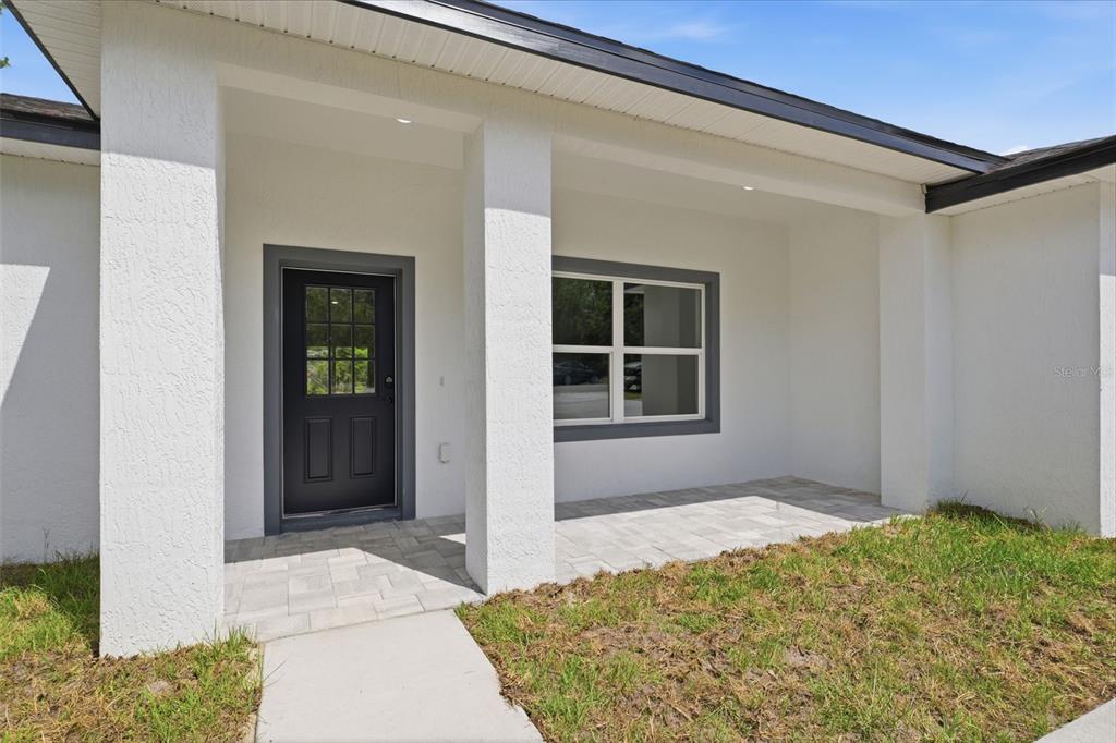 A white stucco house exterior features a covered porch with pavers and a black door — 7712 N TIDE POINT, CITRUS SPRINGS, FL