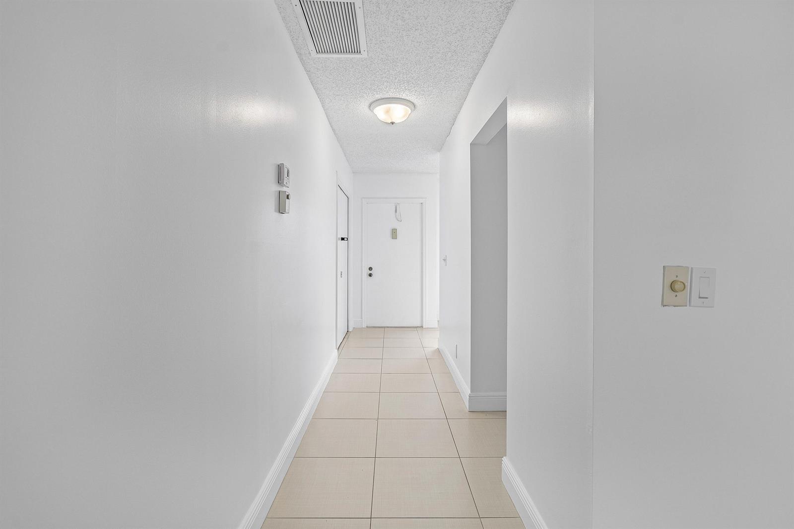 A white hallway features tiled flooring, a ceiling light, and a closed door at the end — 1021 Flame Vine Avenue # 104, Delray Beach FL 33445, DELRAY BEACH, FL