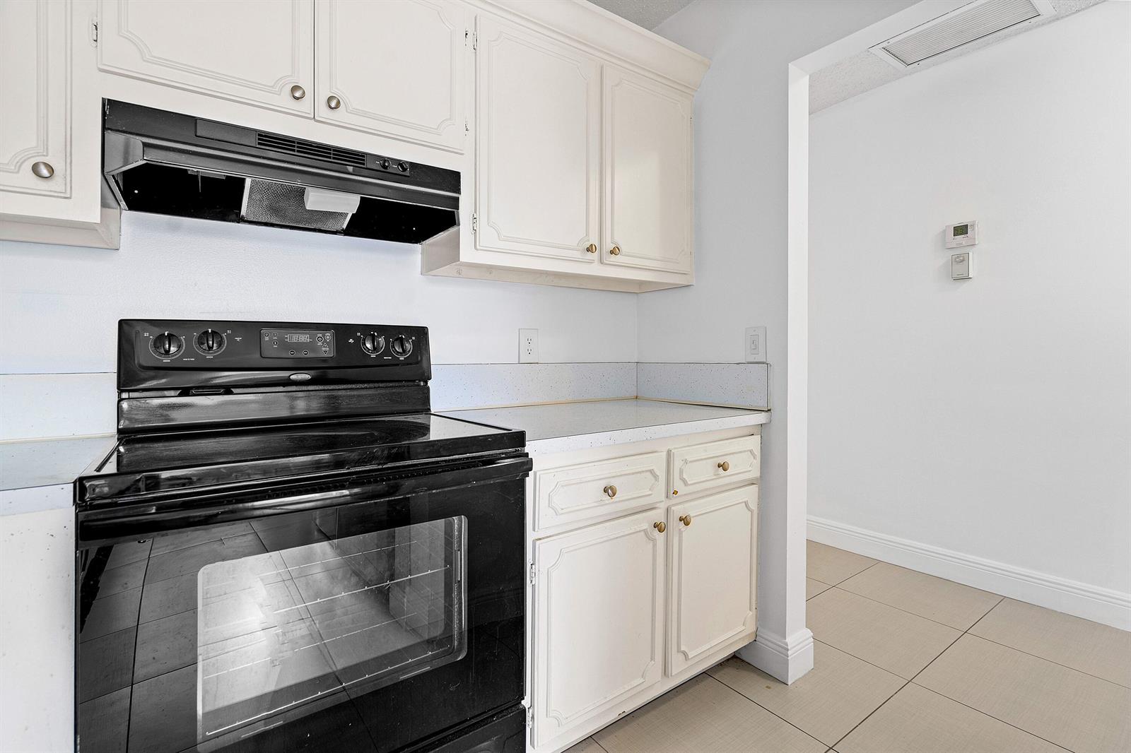 A kitchen features white cabinets, a black stove, and light-colored tile flooring — 1021 Flame Vine Avenue # 104, Delray Beach FL 33445, DELRAY BEACH, FL