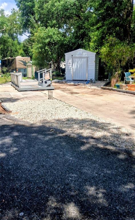 A white storage shed sits on a concrete pad next to a wooden deck — 25225 141ST LANE NE, FORT MC COY, FL