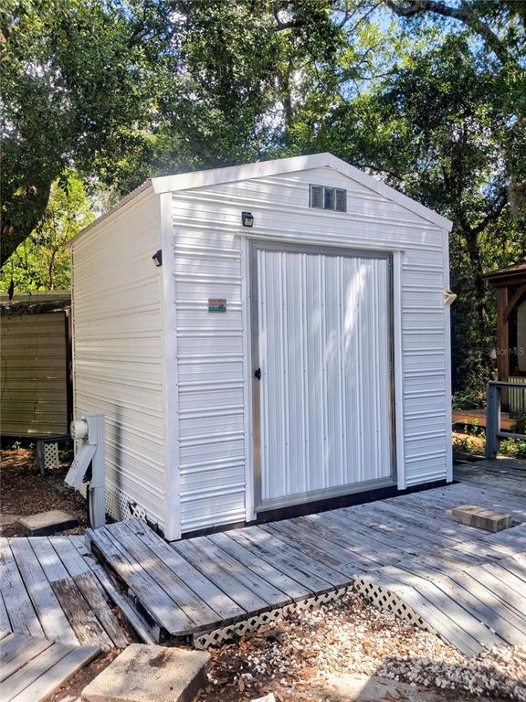 A white metal storage shed stands on a weathered wooden deck in a wooded area — 25225 141ST LANE NE, FORT MC COY, FL