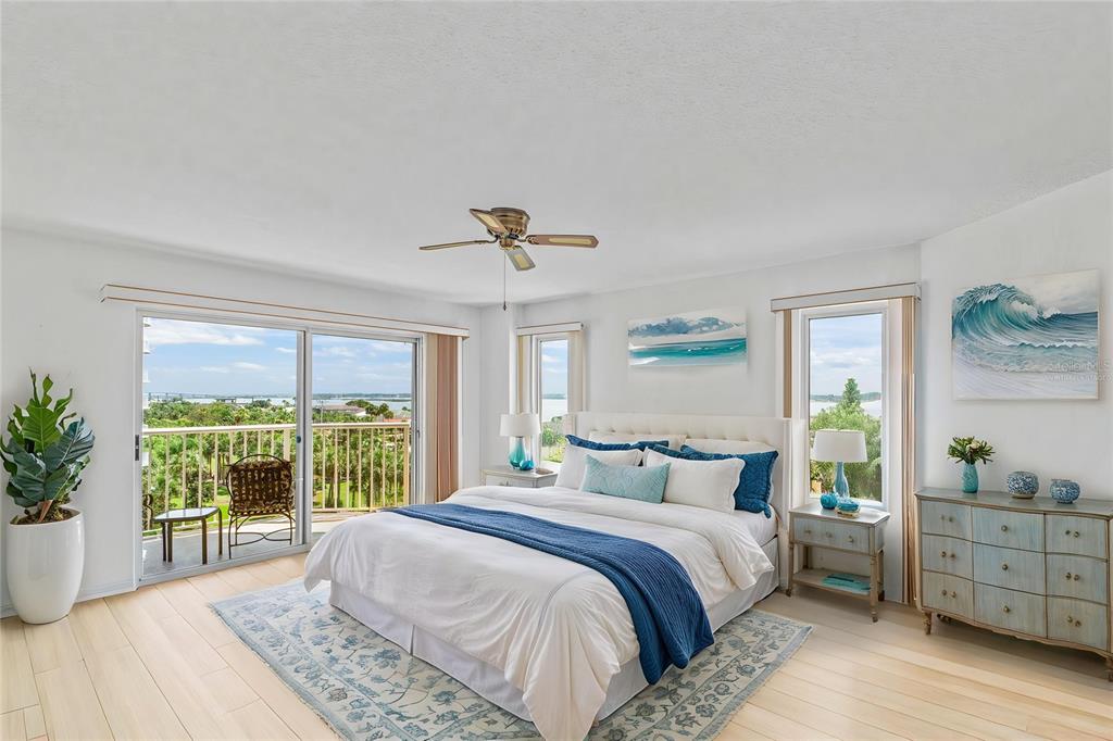 A bright bedroom features a king bed, light wood floors, and a balcony overlooking water — 3 OCEANS WEST BOULEVARD UNIT 6C4, DAYTONA BEACH SHORES, FL