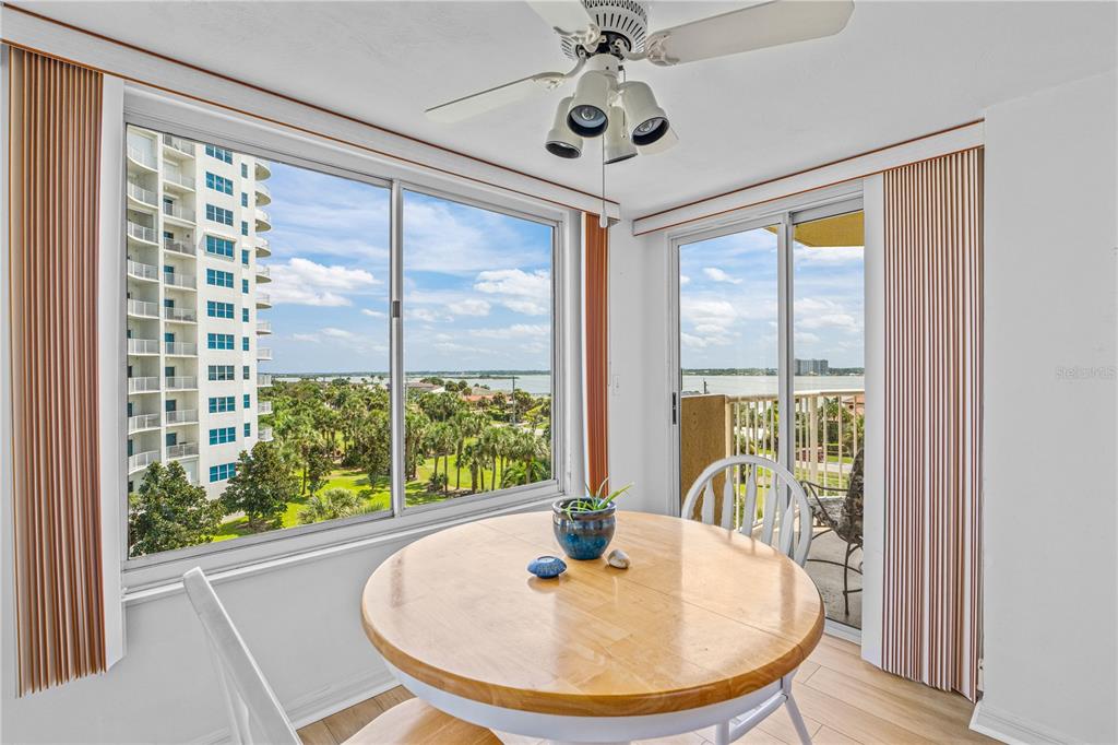 A dining area features a round wooden table, a ceiling fan, and large windows overlooking water — 3 OCEANS WEST BOULEVARD UNIT 6C4, DAYTONA BEACH SHORES, FL