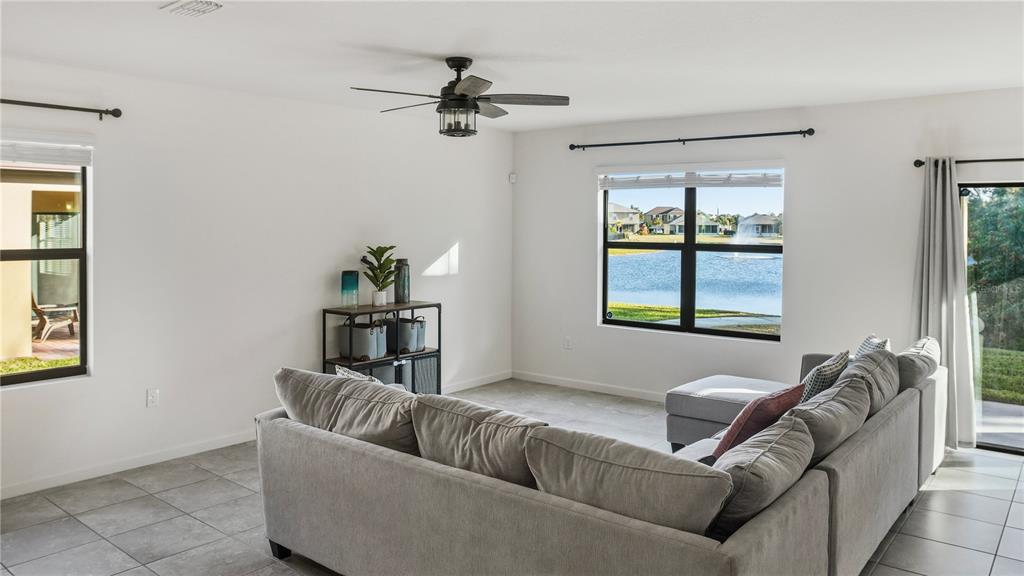 A living room features a gray sectional sofa, tile flooring, and a view of a pond — 5954 ORSINO LANE, COCOA, FL
