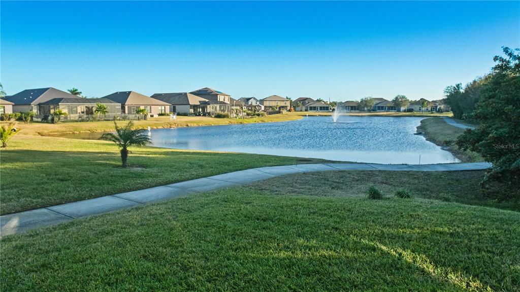 A concrete path winds through a grassy lawn toward a pond with a fountain — 5954 ORSINO LANE, COCOA, FL