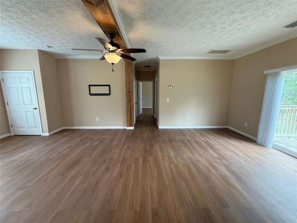 An empty living room features wood-look flooring, a ceiling fan, and a wooden support beam — 11970 OSPREY AVENUE, WEEKI WACHEE, FL