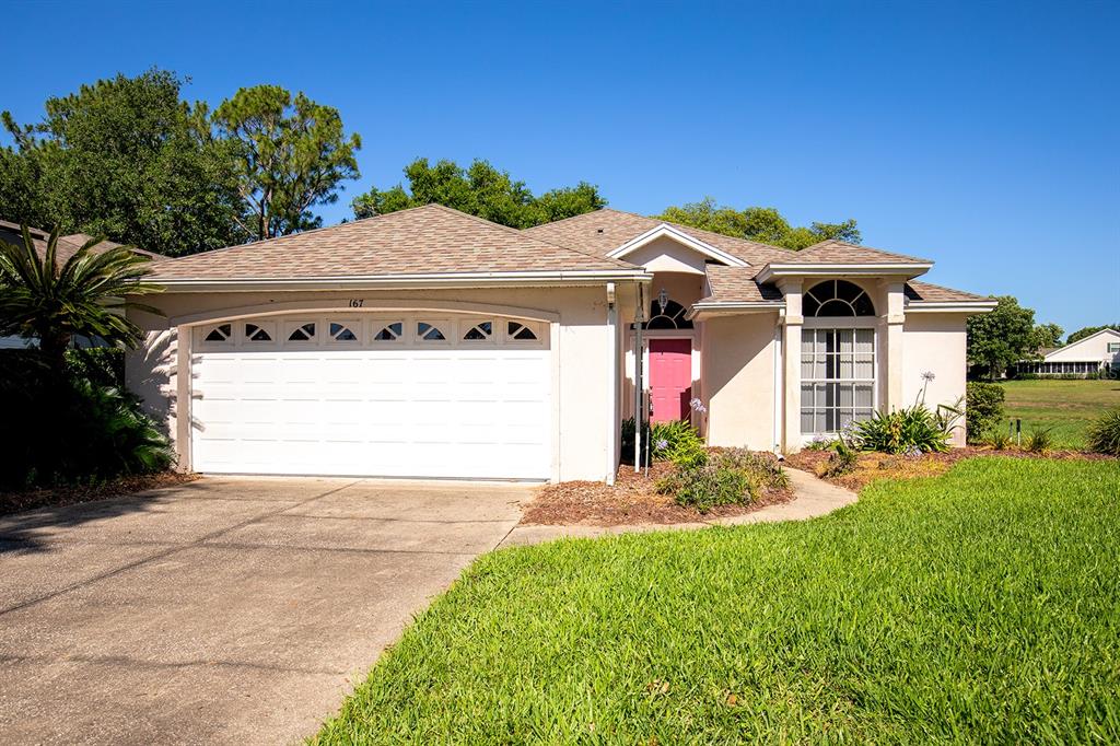 A single-story house with a white garage, pink front door, and a grassy front yard — 167 JUNIPER WAY, TAVARES, FL