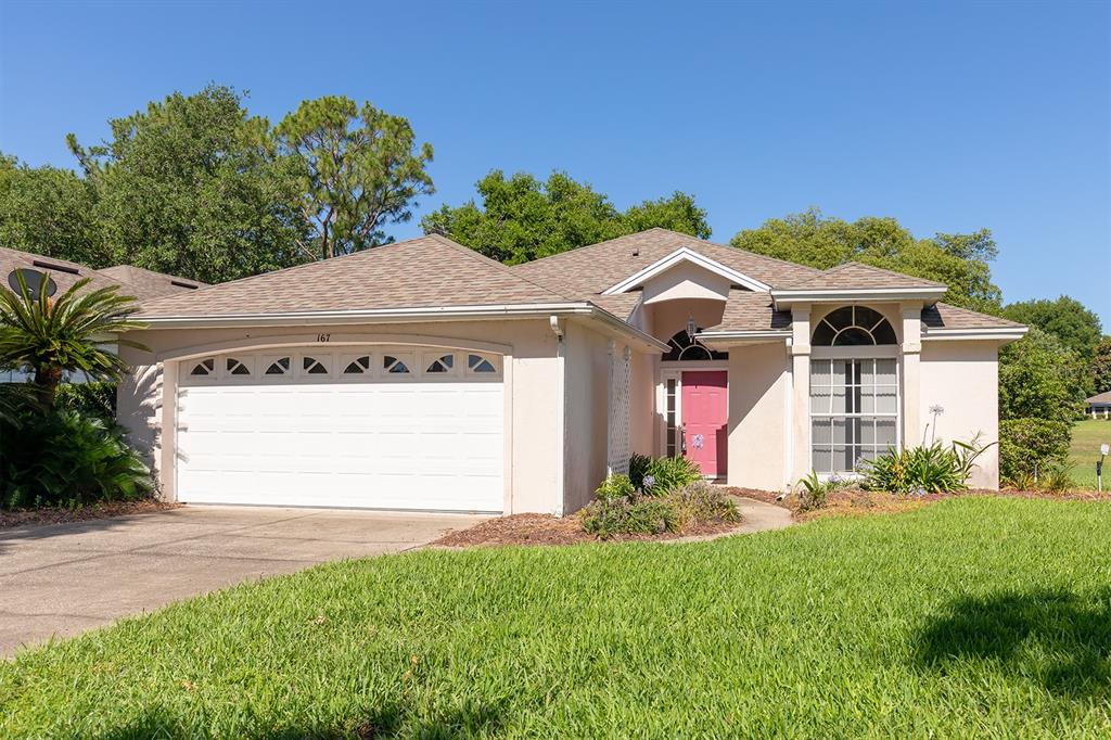 A single-story house with a white garage, pink front door, and a grassy front lawn — 167 JUNIPER WAY, TAVARES, FL