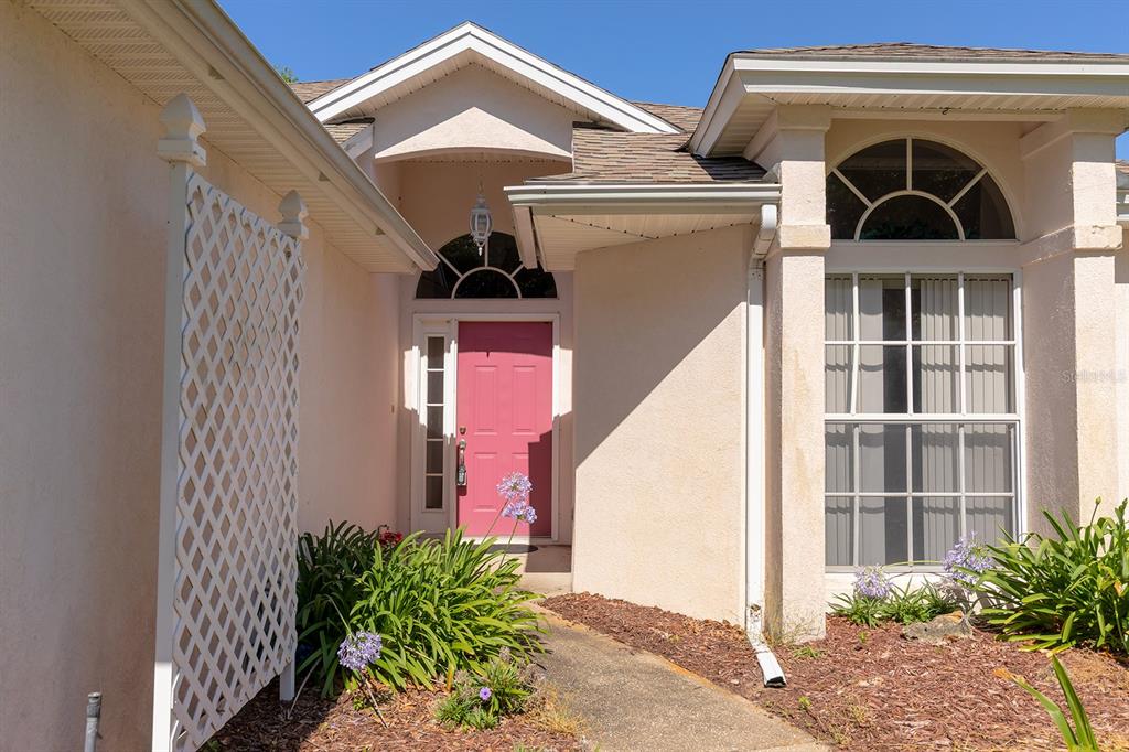 The exterior of a house features a pink front door and a white lattice screen — 167 JUNIPER WAY, TAVARES, FL