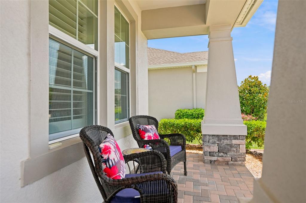 A covered porch features two wicker chairs with floral cushions and a stone-based pillar — 5271 CAPPLEMAN LOOP, BROOKSVILLE, FL