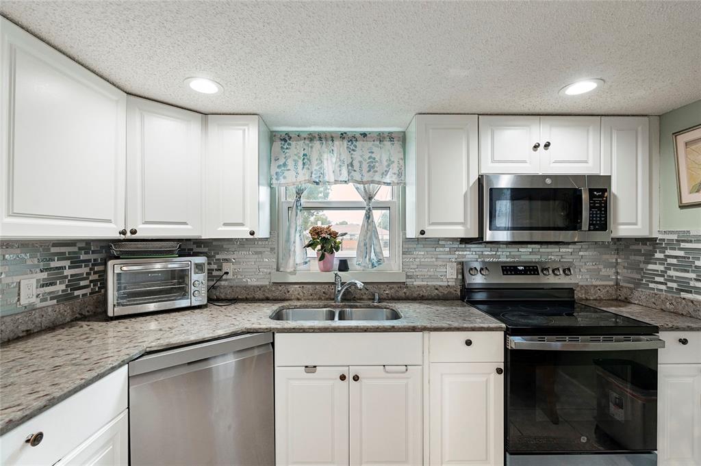 A kitchen features white cabinets, stainless steel appliances, a tiled backsplash, and granite countertops — 7067 JARVIS ROAD, SARASOTA, FL