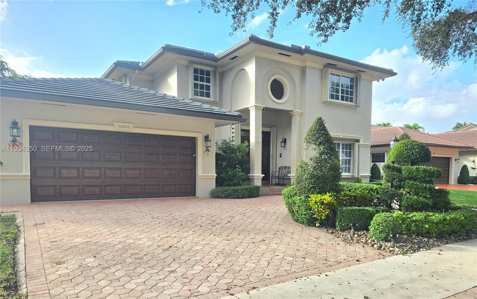 A two-story house features a paved driveway, a dark garage door, and manicured landscaping — 16422 NW 83rd Pl, Miami Lakes FL 33016, MIAMI LAKES, FL