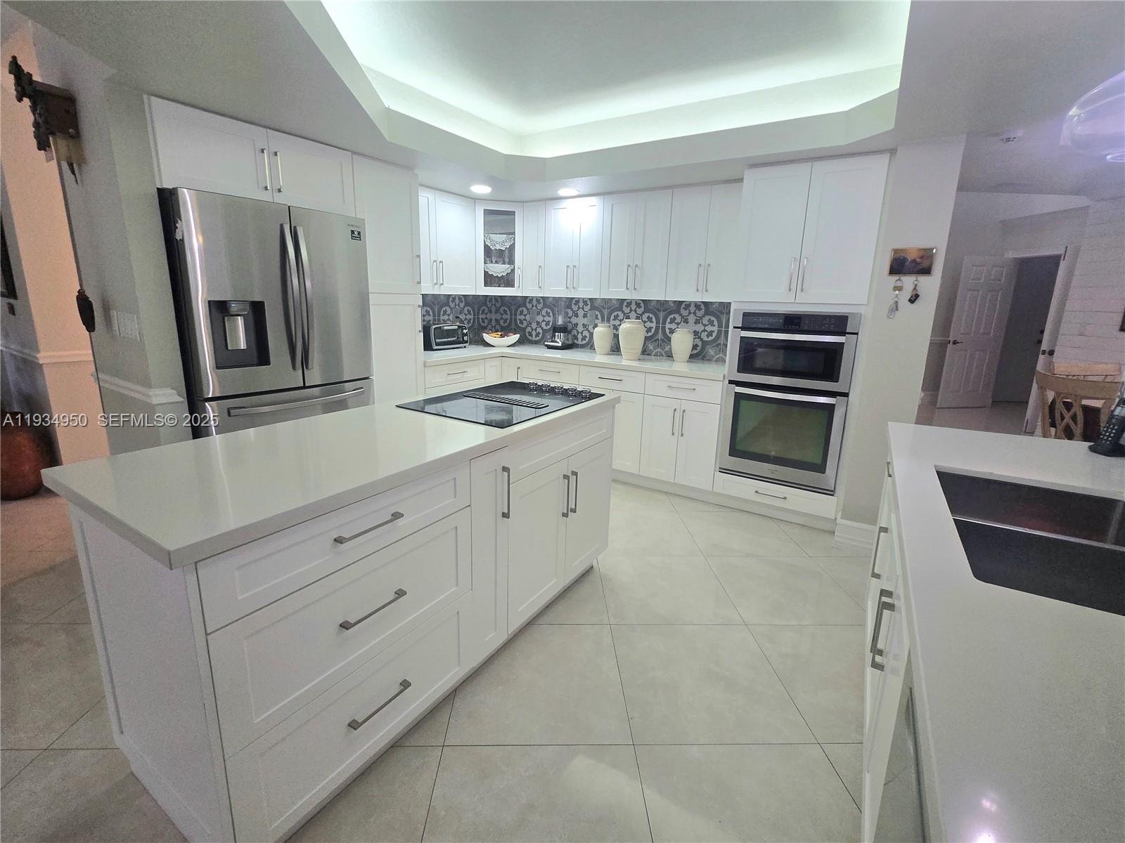 A modern kitchen features white cabinetry, stainless steel appliances, a center island, and tile flooring — 16422 NW 83rd Pl, Miami Lakes FL 33016, MIAMI LAKES, FL