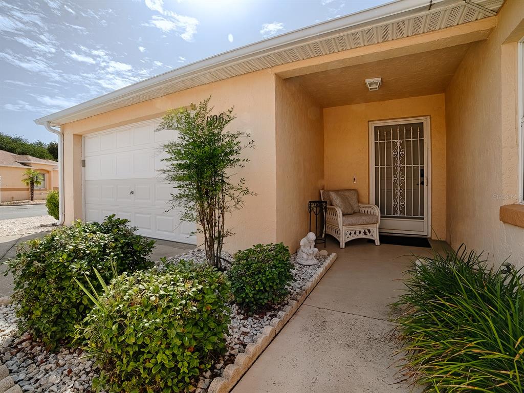A beige house exterior features a garage, a covered entryway, and a landscaped front yard — 1106 RICARDO AVENUE, THE VILLAGES, FL