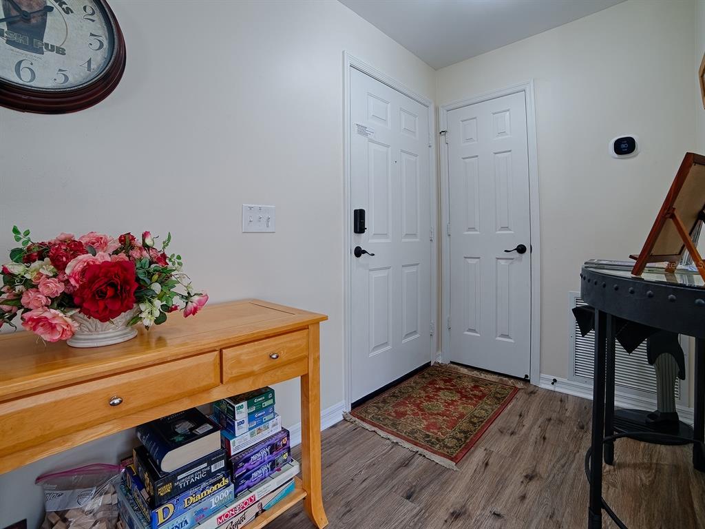 An entryway features a wooden console table, a wall clock, two white doors, and flooring — 1106 RICARDO AVENUE, THE VILLAGES, FL