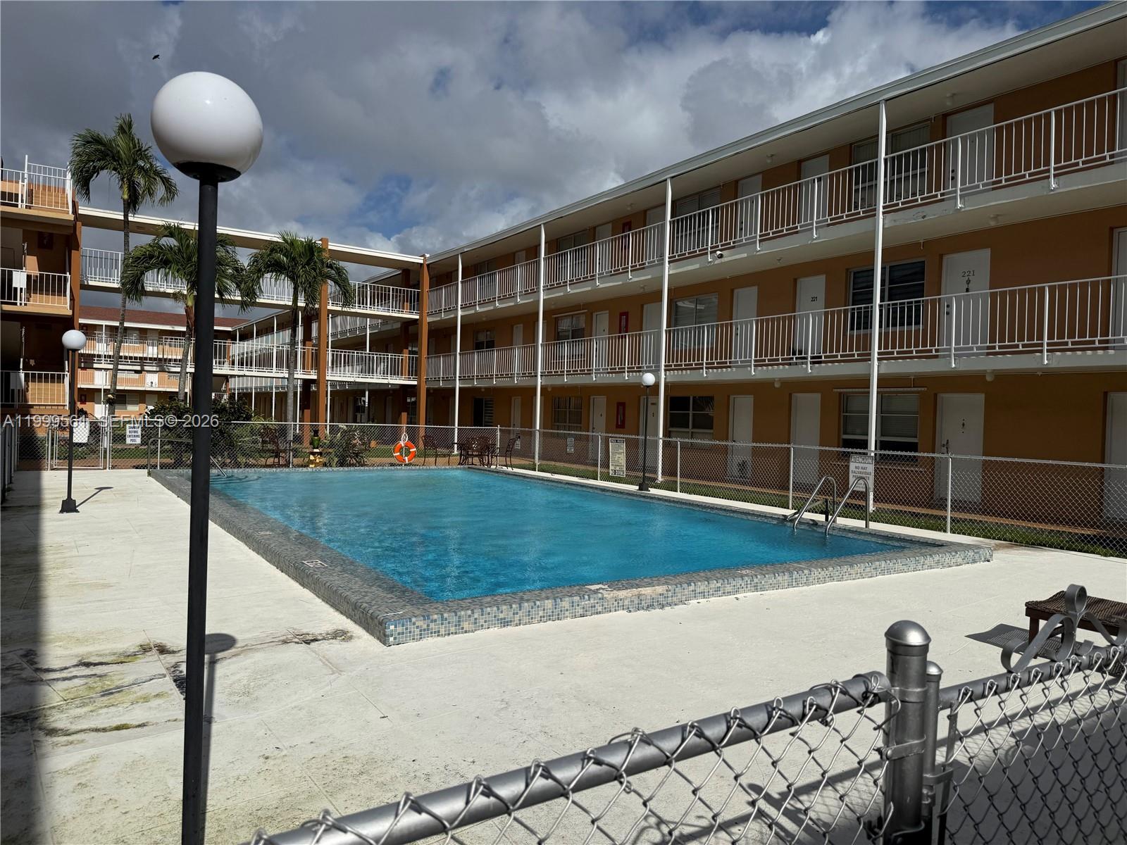 A swimming pool sits in front of a multi-story apartment building with exterior walkways — 3881 W Flagler St # 319, Miami FL 33134, MIAMI, FL