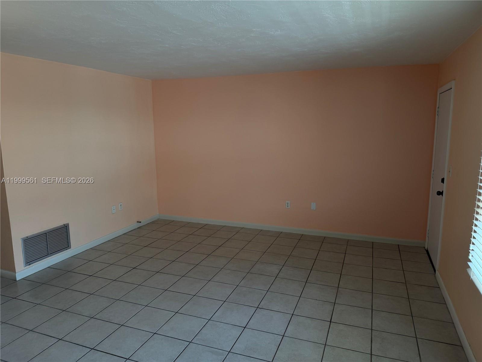 An empty room features peach walls, light-colored floor tiles, a white door, and a vent — 3881 W Flagler St # 319, Miami FL 33134, MIAMI, FL